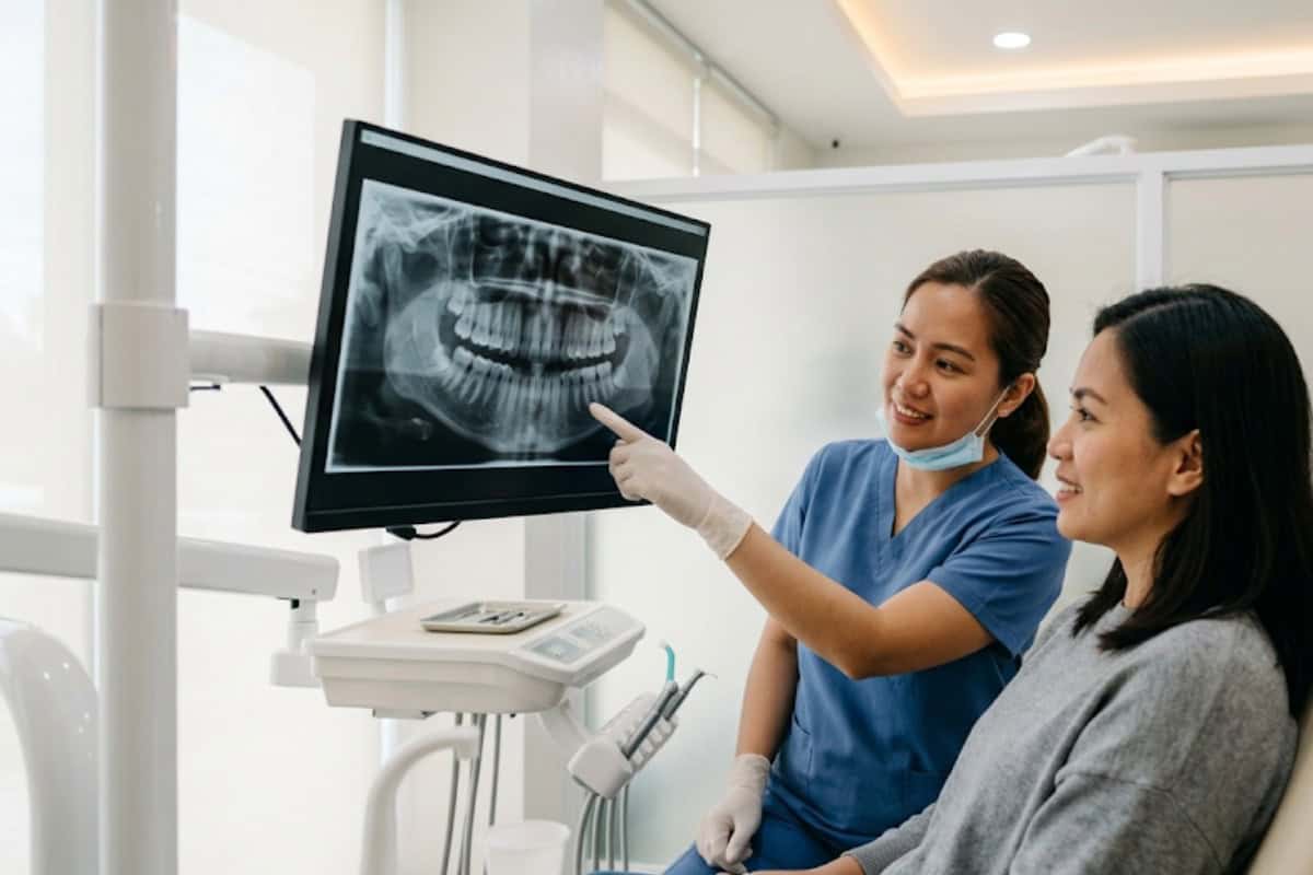 dentist in blue scrubs shows patient a dental X-ray on a monitor in a clinic, both smiling and seated side by side