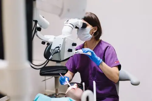 Clinician in purple scrubs and a mask working on a patient through a dental operating microscope.