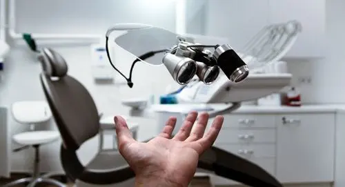 Pair of dental magnification loupes resting on a stand in a treatment room.