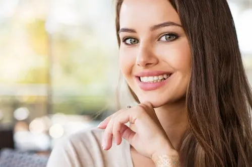 Young woman with long brown hair smiling with her hand resting near her chin.