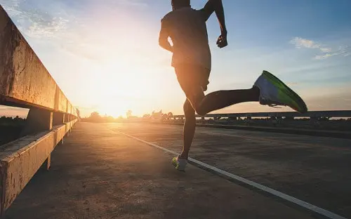 Runner silhouetted against the sunrise on an empty road.