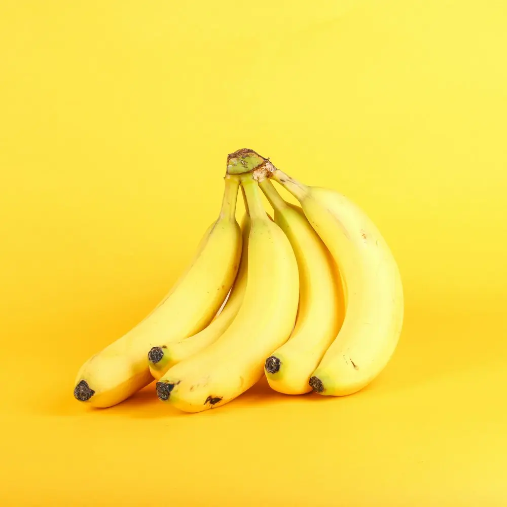 Bunch of ripe bananas against a bright yellow background.
