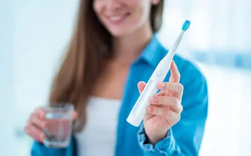 Woman holding an electric toothbrush in one hand and a glass of water in the other.