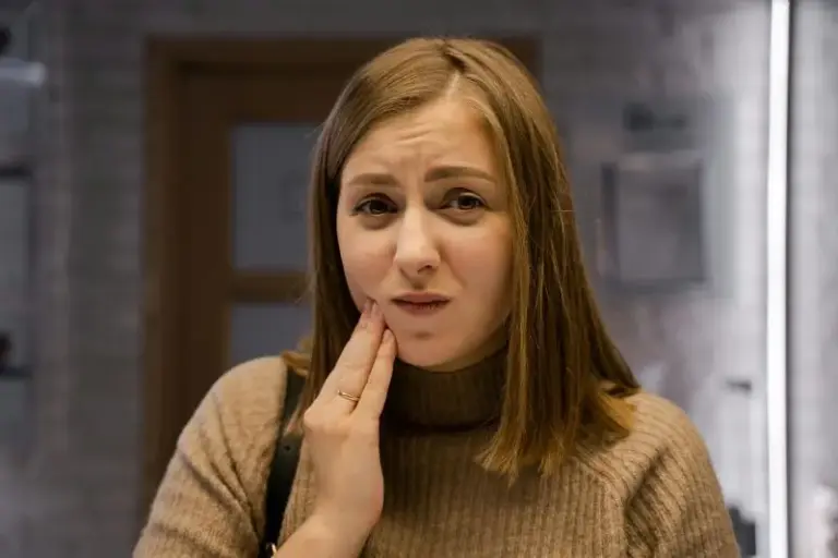 Close-up of a woman in a brown jumper pressing her fingers to her jaw.