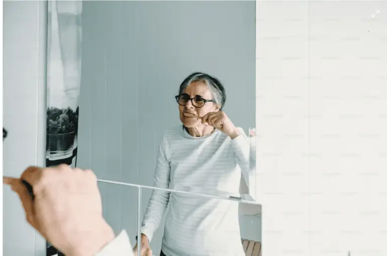 Older woman flossing in a bathroom, seen past the edge of the mirror.