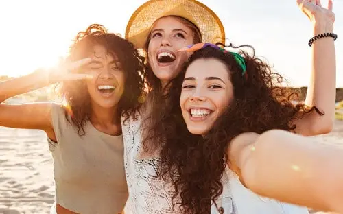 Three young women laughing together outdoors in warm evening light.