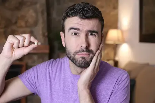 Man in a purple T-shirt holding his jaw with one hand and a length of floss in the other.