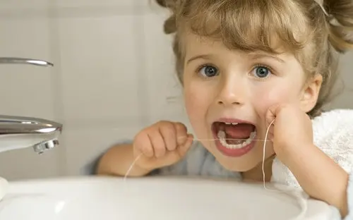Young child flossing at a bathroom mirror with a wide open mouth.