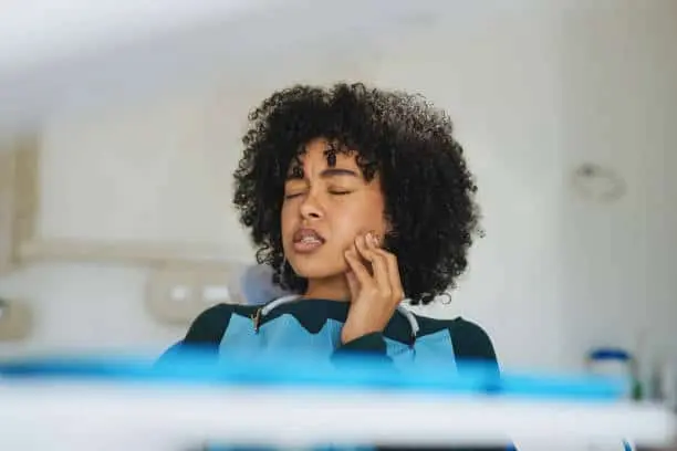 Woman in a dental chair wincing with her hand against her jaw.