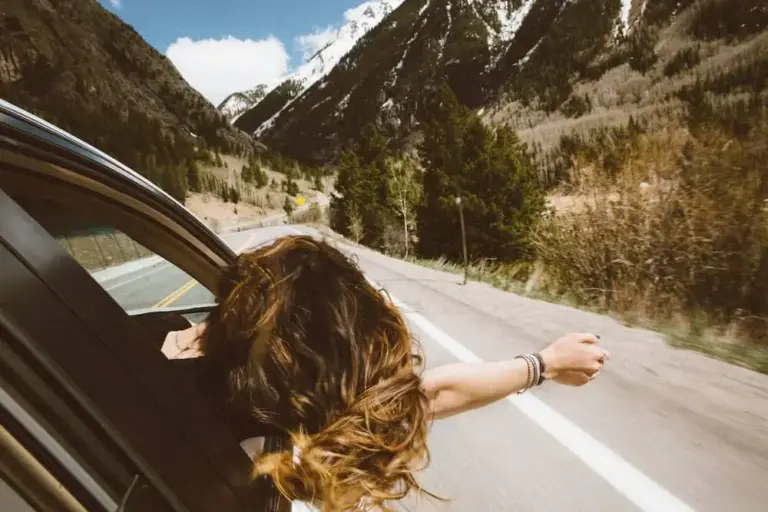 Passenger reaching an arm out of a moving car window on a scenic road.