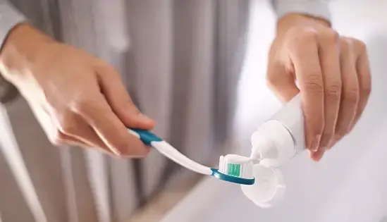 Hand squeezing toothpaste onto a toothbrush.