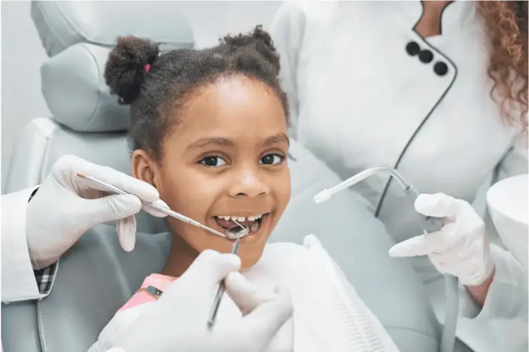 Girl in the dental chair laughing while a clinician examines her teeth.