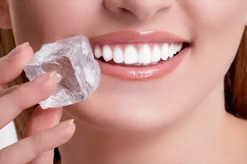 Close-up of a woman holding a large ice cube beside her smile.