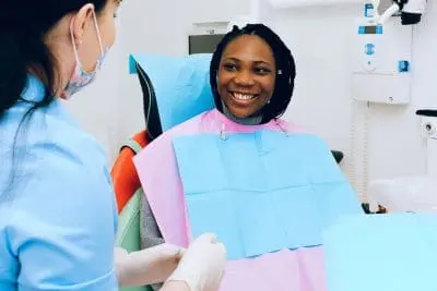 Smiling woman in a pink bib seated in the dental chair beside a clinician.
