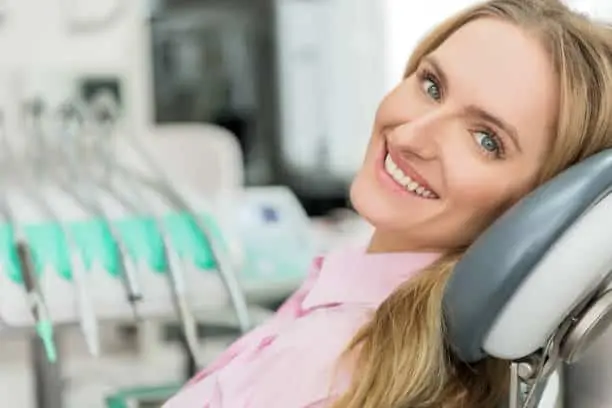 Blonde woman in a pink shirt smiling while seated in a dental chair.