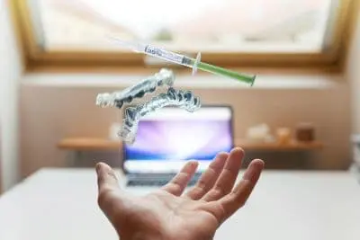 Hand held out beneath a composite image of clear aligners above a laptop.