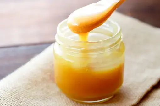Spoon lifting honey from an open glass jar.