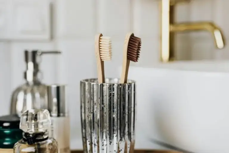Toothbrushes in a glass tumbler on a bathroom counter beside a soap dispenser.