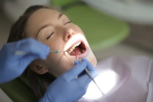 Gloved hands holding instruments in a reclining patient's open mouth.