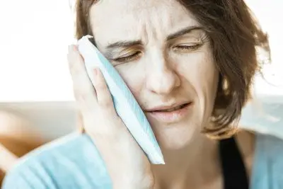 Woman pressing a folded cloth compress against her cheek.