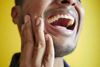 Man against a yellow background with his mouth open, holding his jaw.