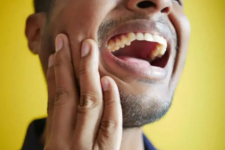 Man holding his jaw with his mouth open against a yellow background.
