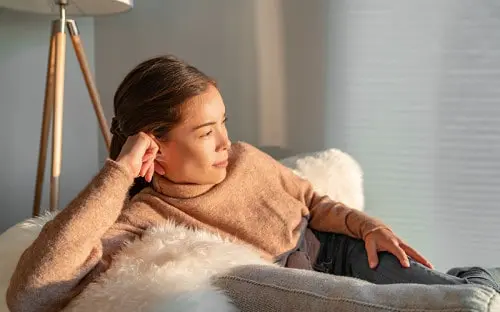 Woman lying on a sofa with her hand held against her ear and jaw.