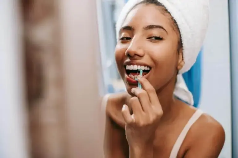 Woman in a hair towel using a floss pick and smiling.