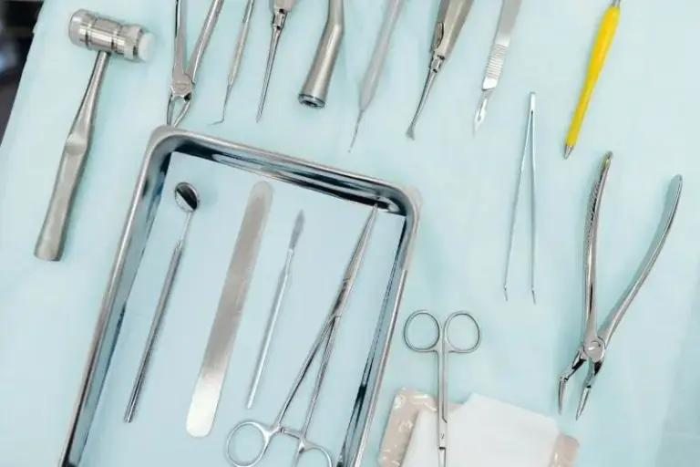 Dental instruments and extraction forceps arranged on a teal surface.