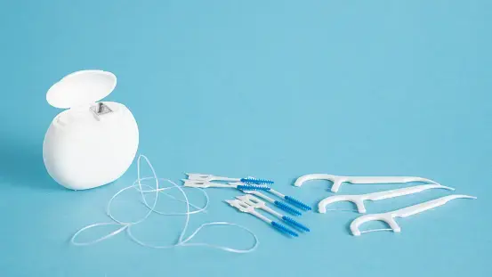 Interdental brushes, floss picks and a length of floss laid out on a blue background.