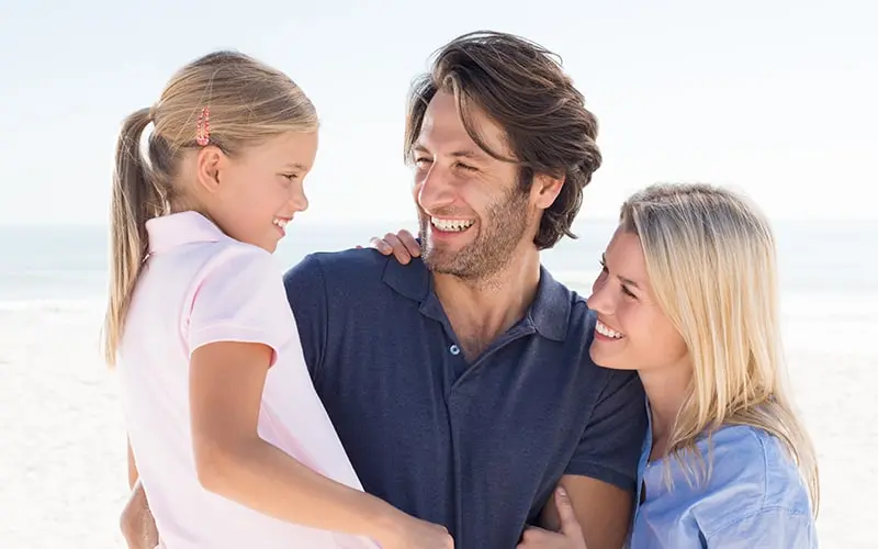 Family of three smiling together at the beach.
