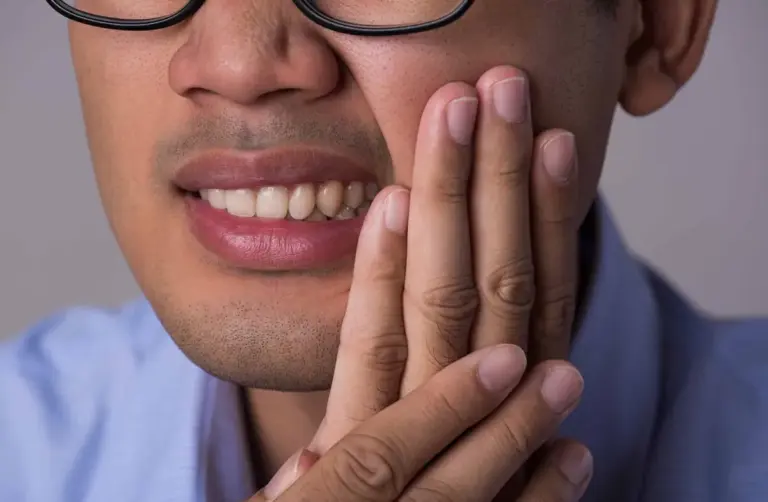 Man in glasses holding his hand against his cheek and jaw.
