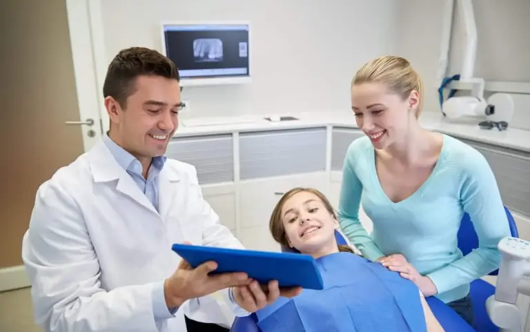 Dentist showing a tablet to a girl in the chair with her mother beside her.