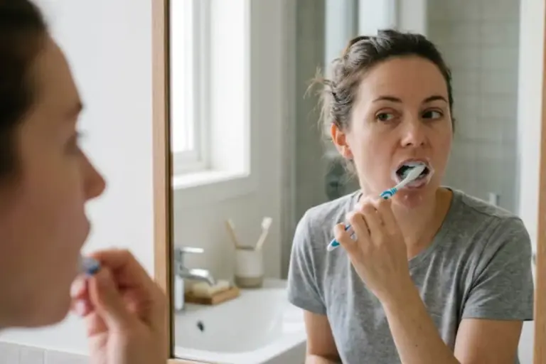Woman brushing her teeth in front of a bathroom mirror.