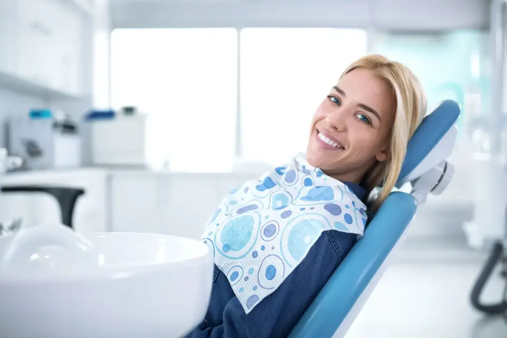 A woman smiling in a dental chair wearing a bib
