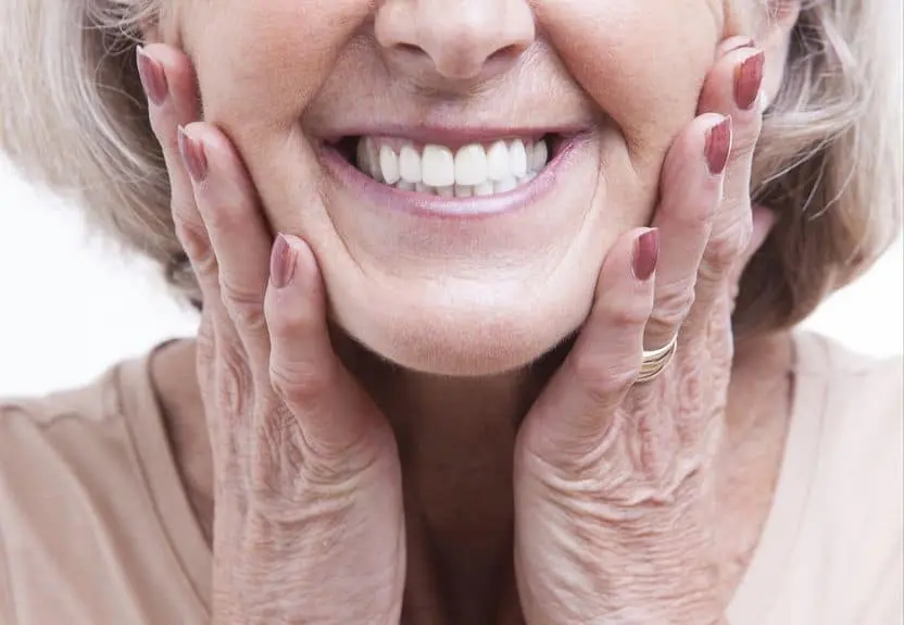 An older woman smiling with her hands resting on her cheeks