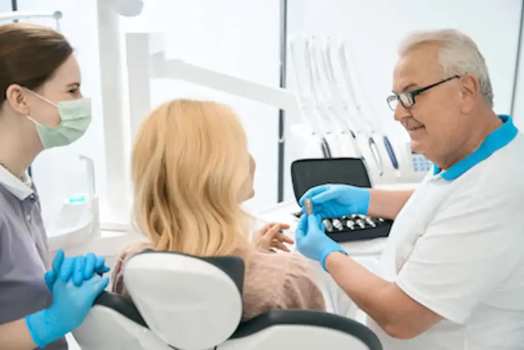 A clinician holding a shade guide beside a patient in the chair